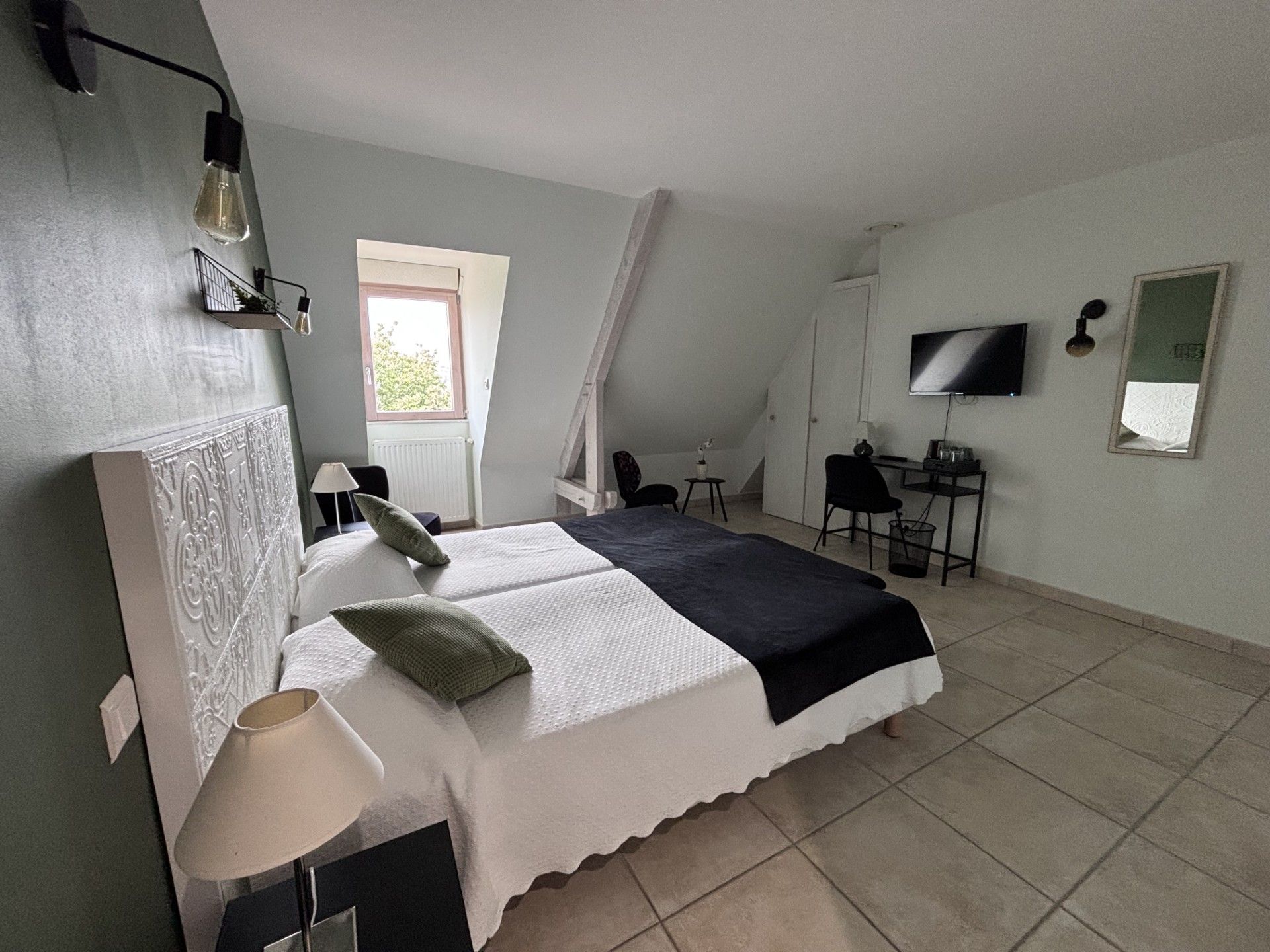 A bedroom with a bed, a desk, a chair, a TV, and a window.