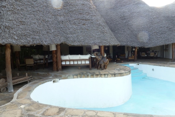 A pool area with a circular pool, thatched-roof structures, and stone flooring.