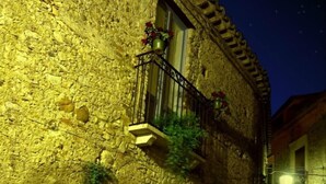 A stone building with a balcony and a window, illuminated by night lighting. - B&B Amphisya (Roccella Jonica)