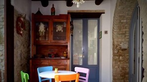 A dining area with a round table, colorful chairs, a wooden cabinet, and a stone wall. - B&B Amphisya (Roccella Jonica)