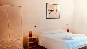 A bedroom with a bed, a wardrobe, a nightstand with a candle, and a wall-mounted abstract art piece. - B&B Amphisya (Roccella Jonica)