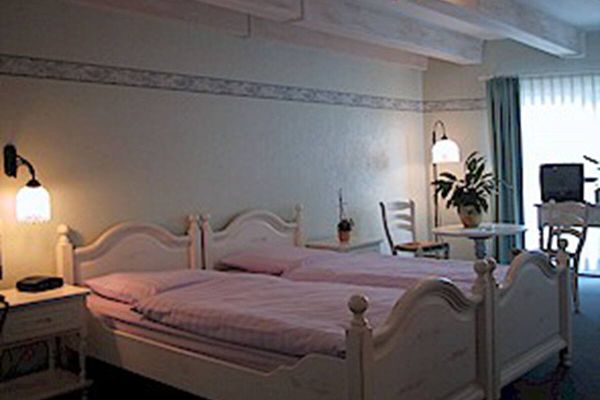 A bedroom with a single bed, bedside table, lamp, chair, and a small table with a plant.