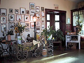A room with a wall adorned with framed pictures, a vintage bicycle, a cart with plants, and a vintage television set.