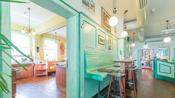 A restaurant with wooden floors, green walls, and a bar area with stools. - Hotel Bergschlösschen (Jueterbog)