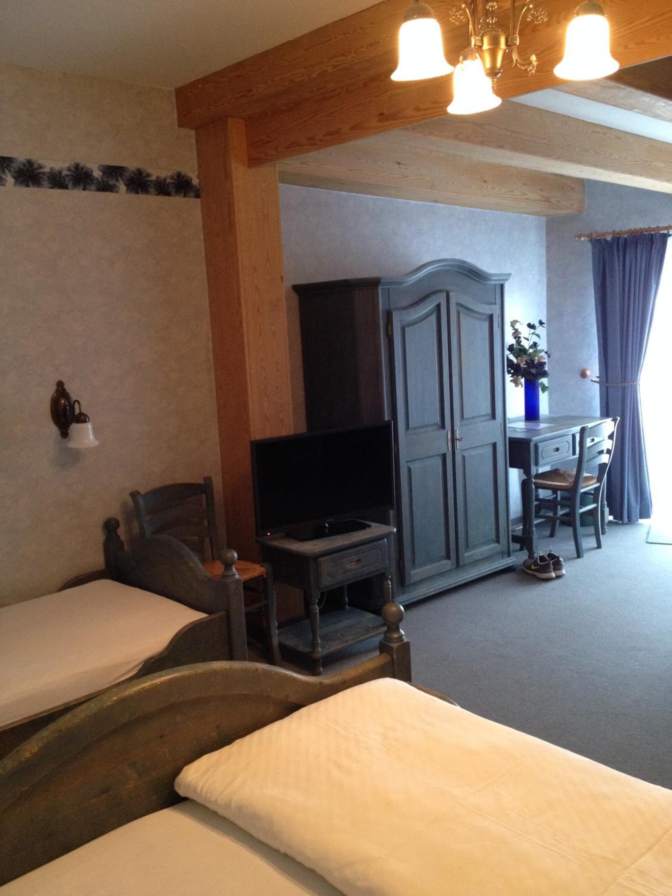 Una habitación con dos camas, televisión, escritorio con silla y ventana con cortinas.
