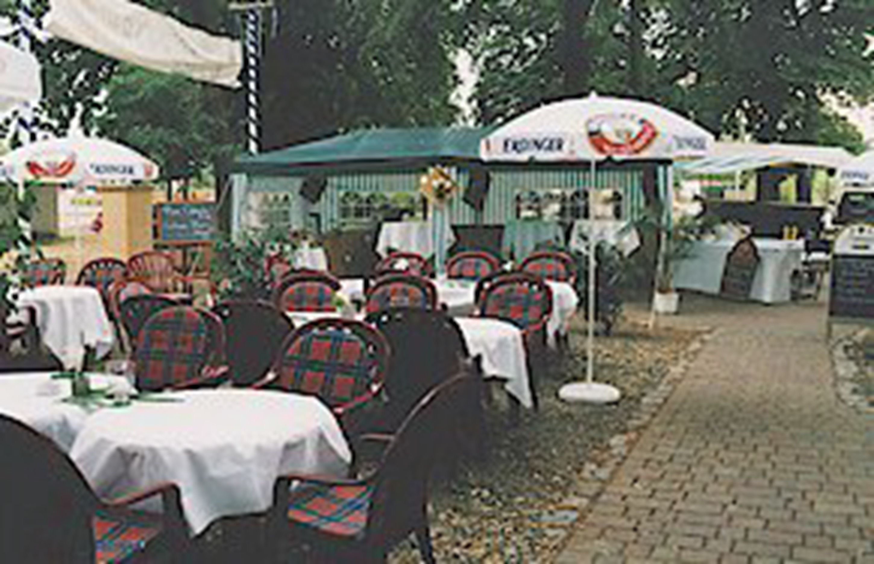 Un espace extérieur aménagé pour les repas, avec des tables, des chaises, des parasols et un chemin en briques.