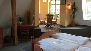 A bedroom with a wooden bed, a desk with a chair, a dining table with chairs, and a potted plant. - Hotel Bergschlösschen (Jueterbog)