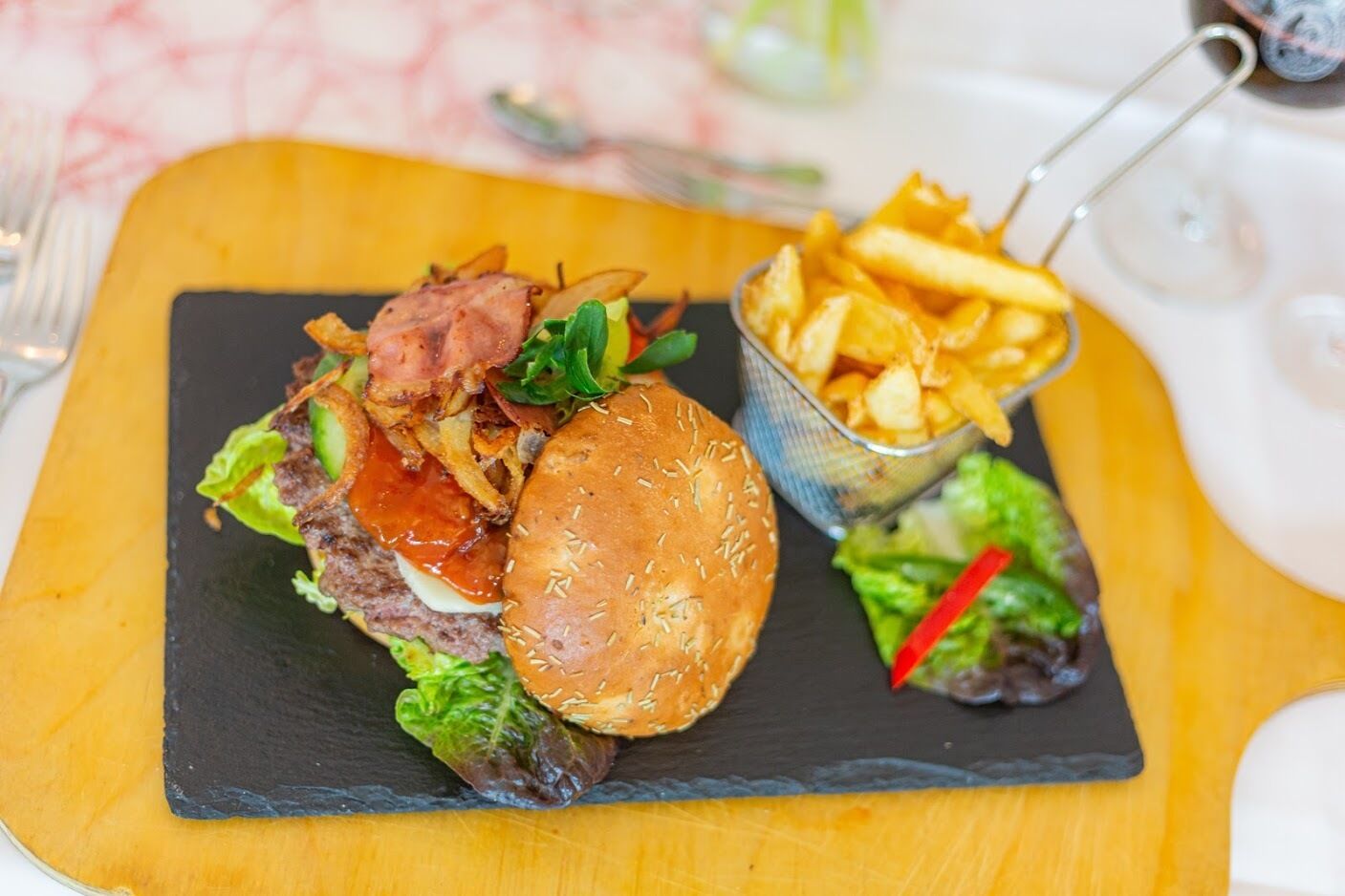 A meal consisting of a burger with lettuce, tomato, and bacon, accompanied by a side of fries and a small salad on a slate board.