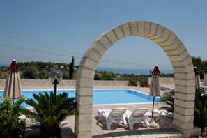 A stone archway leading to a pool area with white lounge chairs and umbrellas, overlooking a scenic landscape.