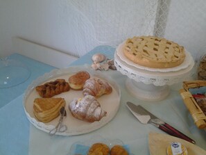 A table with various pastries and a pie on a lace-covered stand.