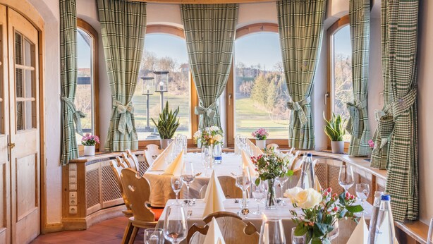 A dining area with a long table set for a meal, large windows with curtains, and a view of the outdoors. - Hotel Gasthof Huber (Ebersberg)