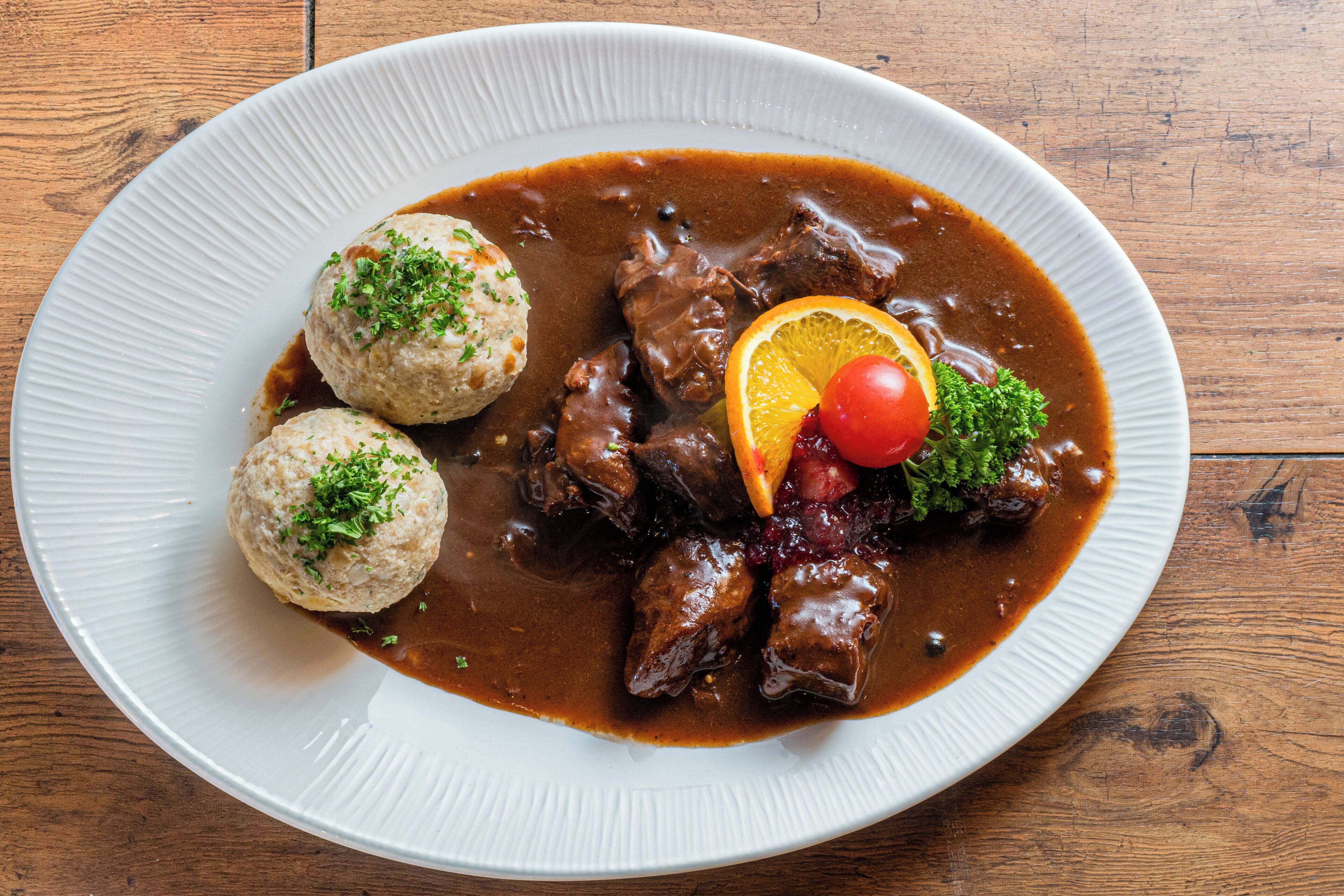 A plate of food with meat, dumplings, and garnishes on a wooden table.