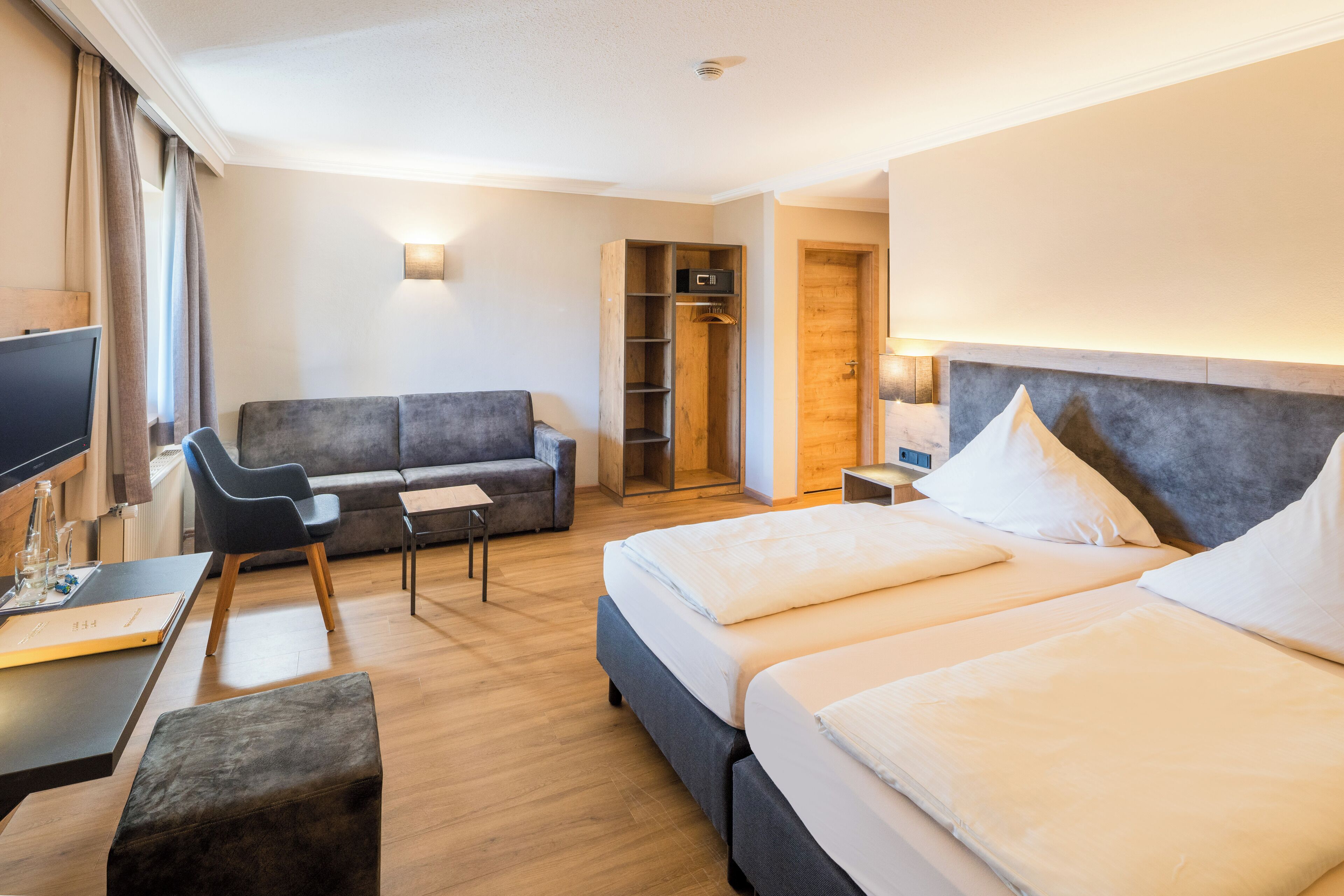 A hotel room with a bed, a sofa, a desk, and a TV.