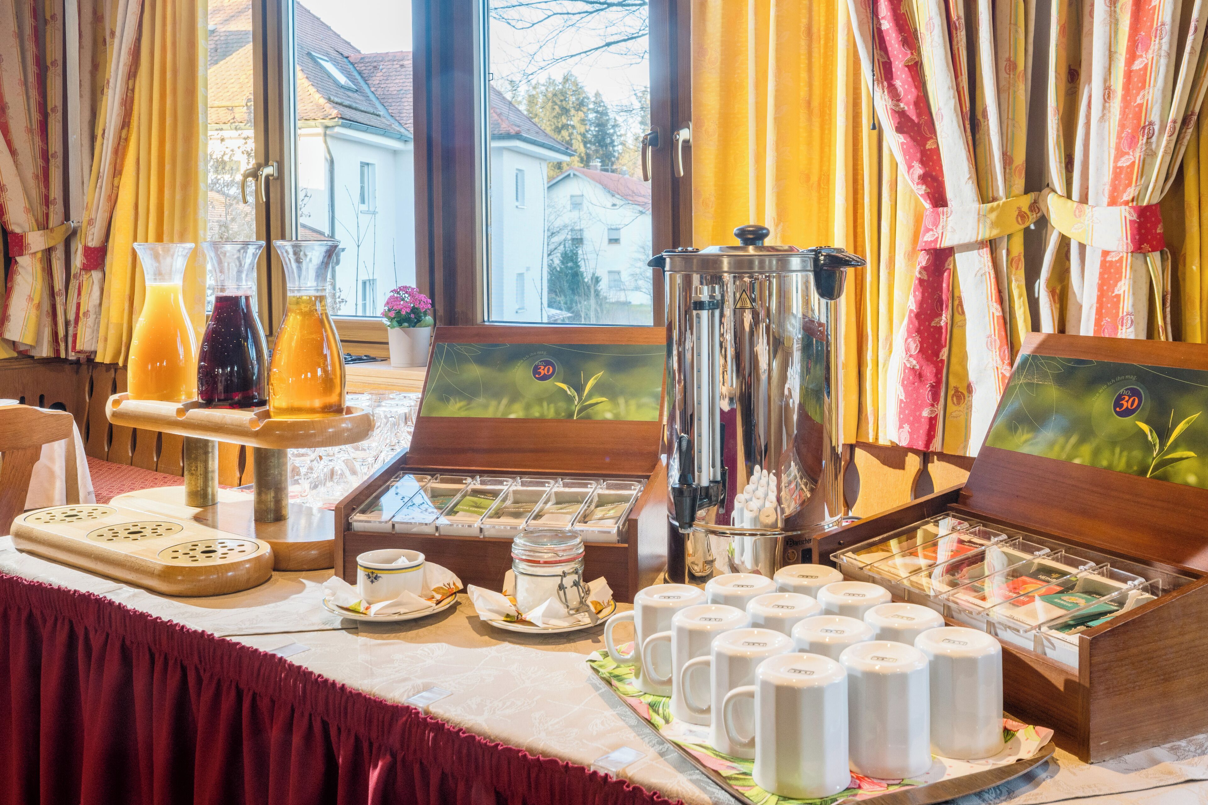 Un bufé de desayuno con diferentes alimentos y bebidas, una máquina de café y vistas al exterior.