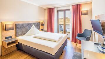 A hotel room with a large bed, a desk with a laptop, a chair, and a TV.