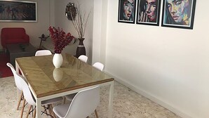 A dining area with a glass-top table, white chairs, a vase with red flowers, and three framed artworks on the wall. - Roma Suites (Mexico City)