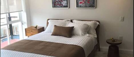 A modern bedroom with a large bed, two wall-mounted artworks, a bedside table, and a round side table.