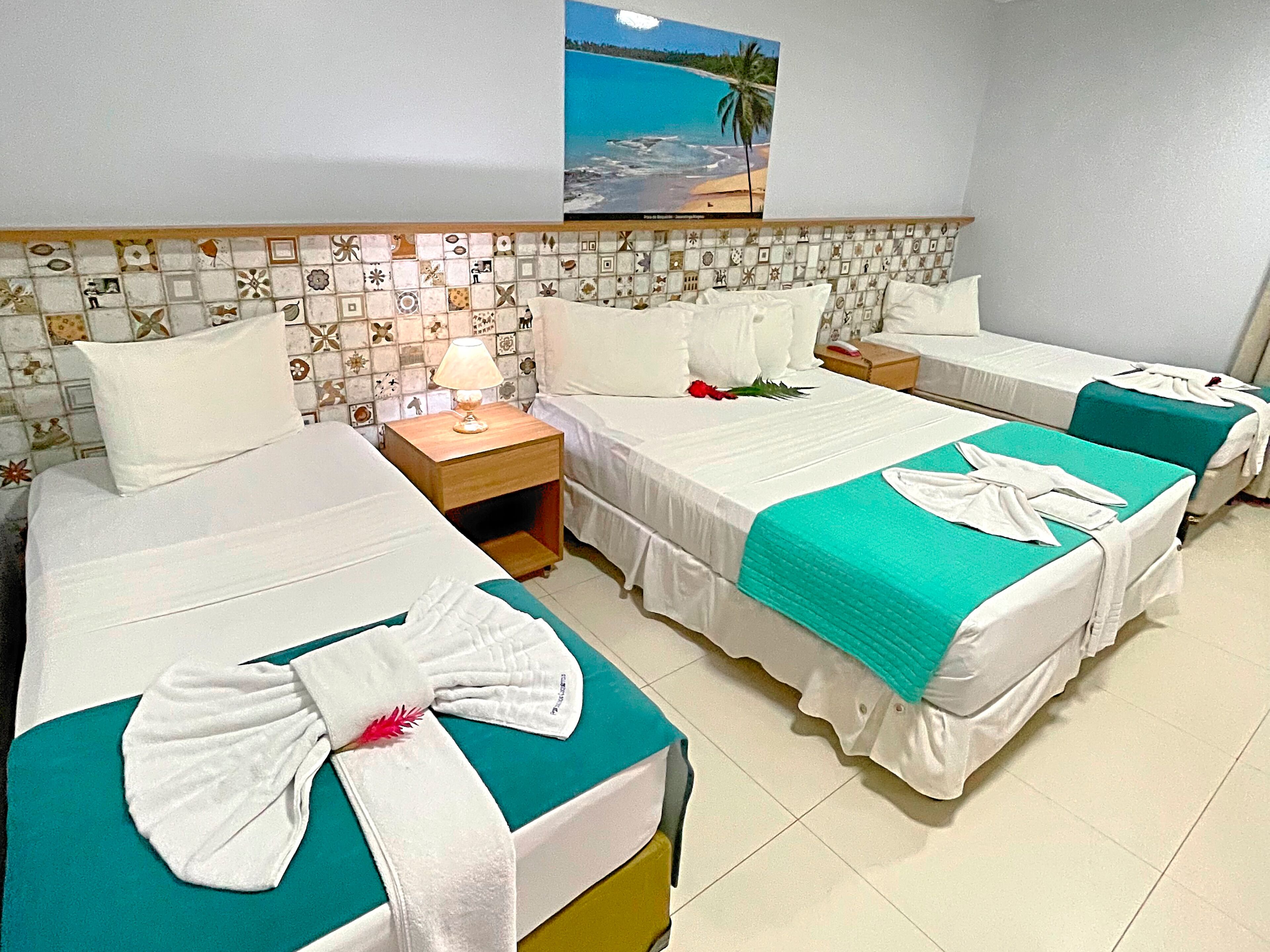 A hotel room with two beds, a nightstand with a lamp, and a wall with a tropical beach picture.