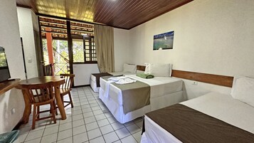 Habitación de hotel con cama, escritorio y silla. Se ve una ventana con cortinas y vistas a árboles.