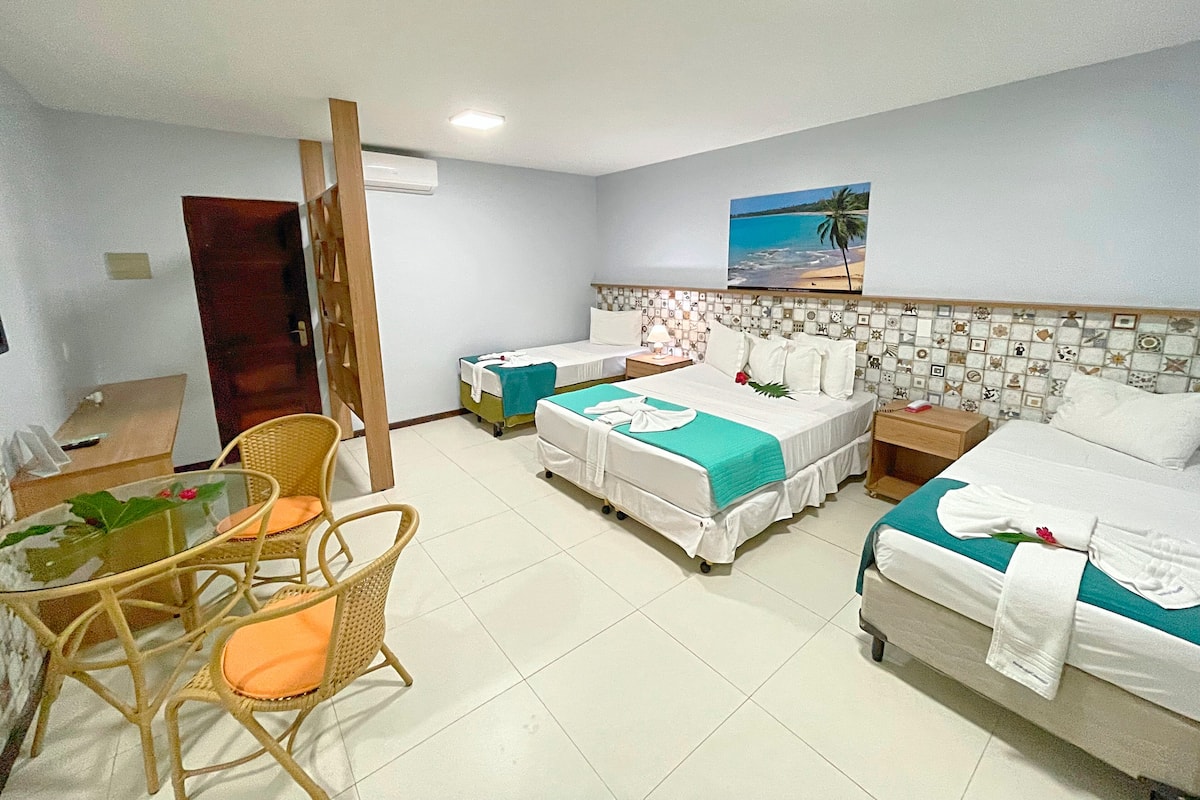 A hotel room with two single beds, a desk with a chair, a small table with a plant, and a wall-mounted TV.