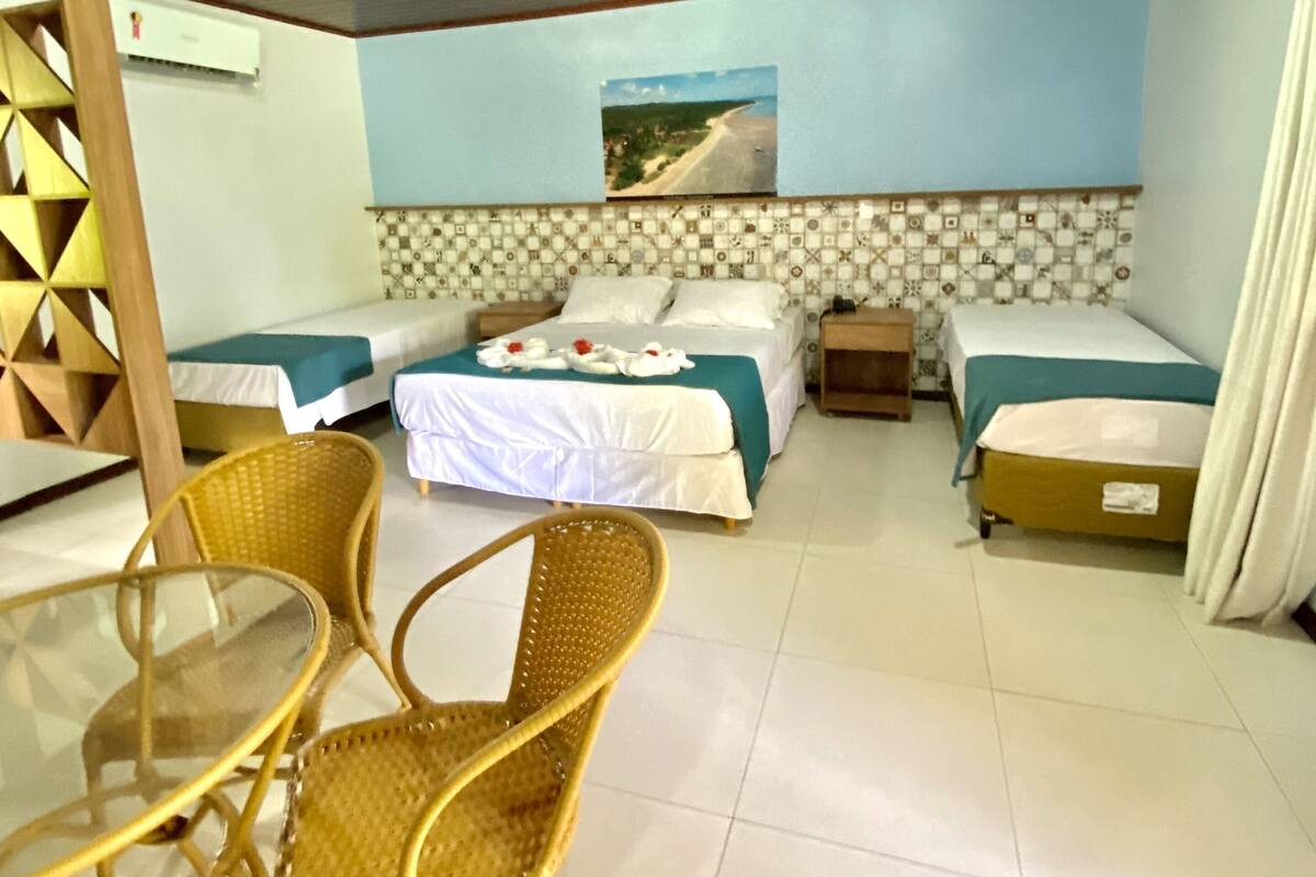 A hotel room with two single beds, a dining table with chairs, a ceiling fan, and a wall-mounted air conditioner.
