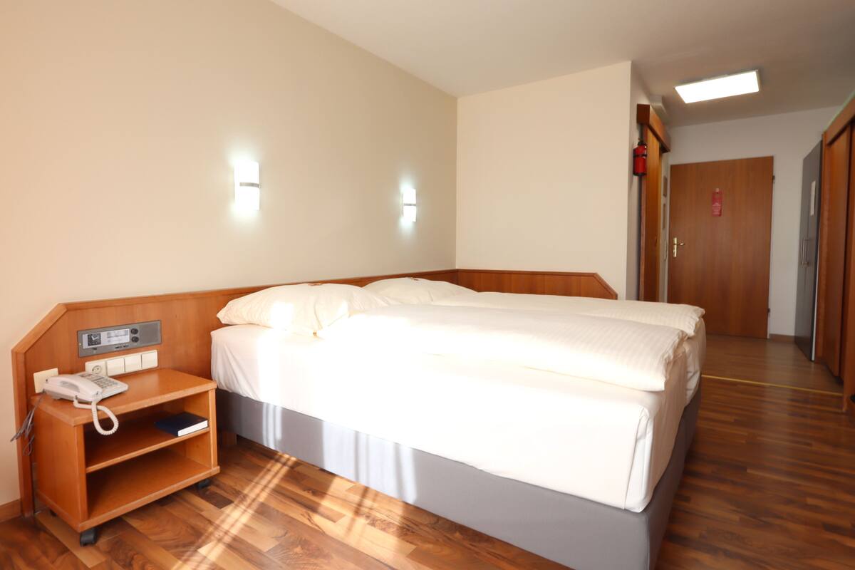 Habitación de hotel con cama doble, teléfono en la mesita de noche, un pequeño estante y suelo de madera.