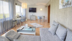 A modern living room with a sofa, a coffee table, a desk, and a TV mounted on the wall. - Kemnater Hof Apartments   (Ostfildern)