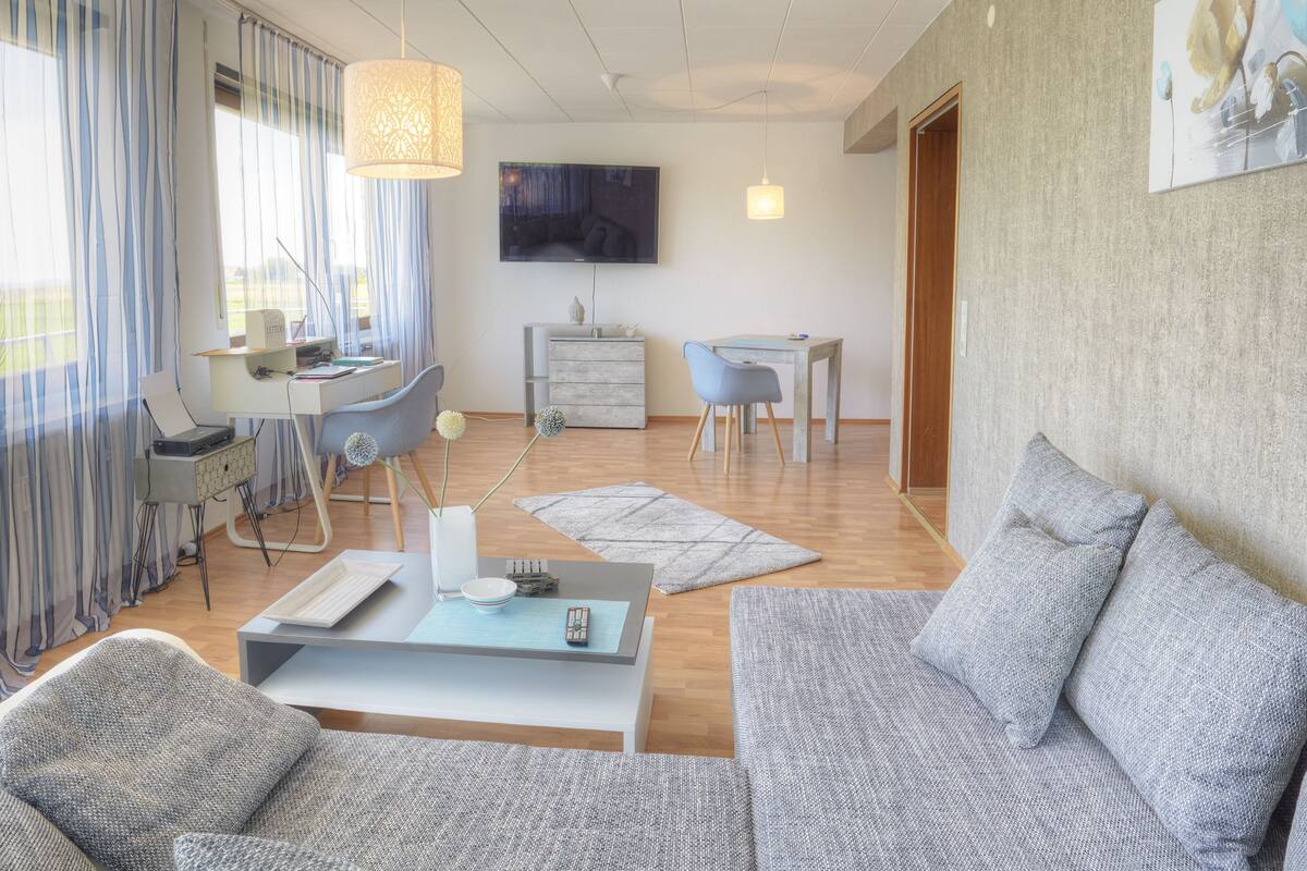 Una sala de estar moderna con un sofá, una mesa de centro, un escritorio y un televisor montado en la pared.