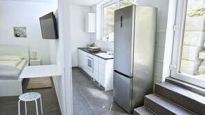 A compact kitchen with a built-in refrigerator, white cabinetry, and a window providing natural light. - Kemnater Hof Apartments   (Ostfildern)