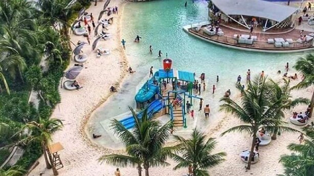 A resort with a large pool, palm trees, and a sandy beach area. - 2 BR Condo by JAD at Azure Urban Resort Residences (Parañaque)