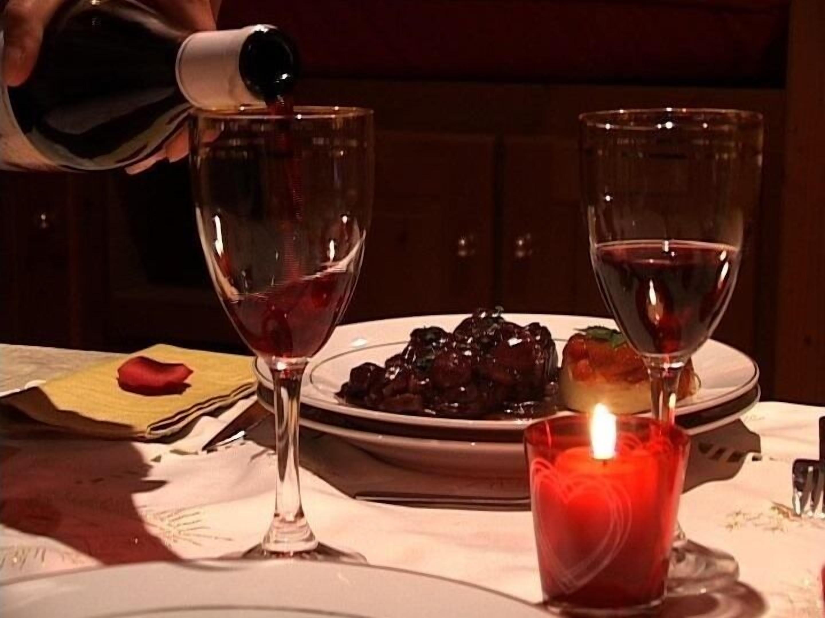 A table with two wine glasses, a candle, and a plate of food.