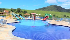 Una piscina amb tobogans i una font d'aigua amb forma de granota, envoltada de gandules i vistes a les muntanyes.