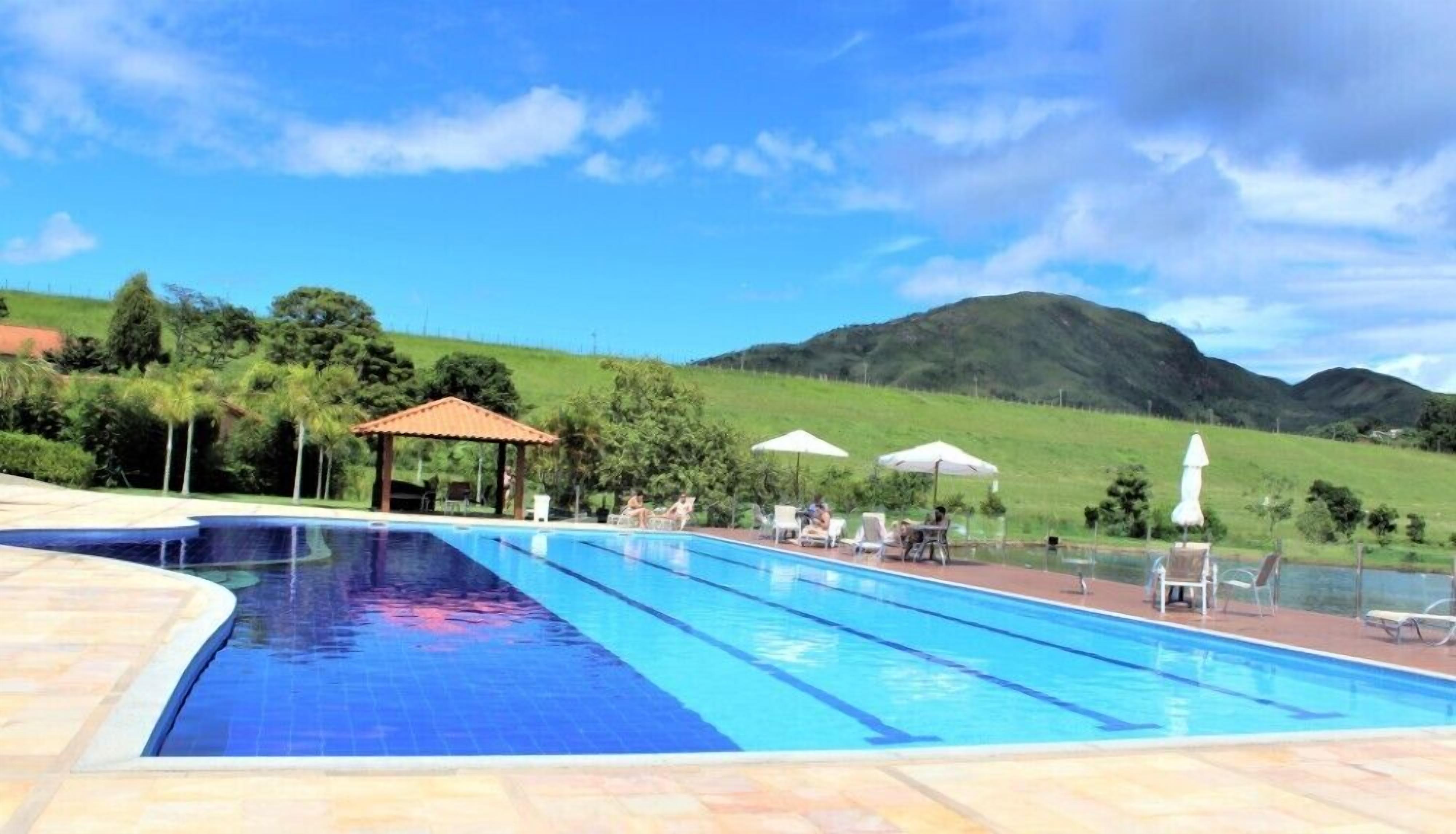Piscina com espreguiçadeiras e guarda-sóis, cercada por vegetação e colinas.