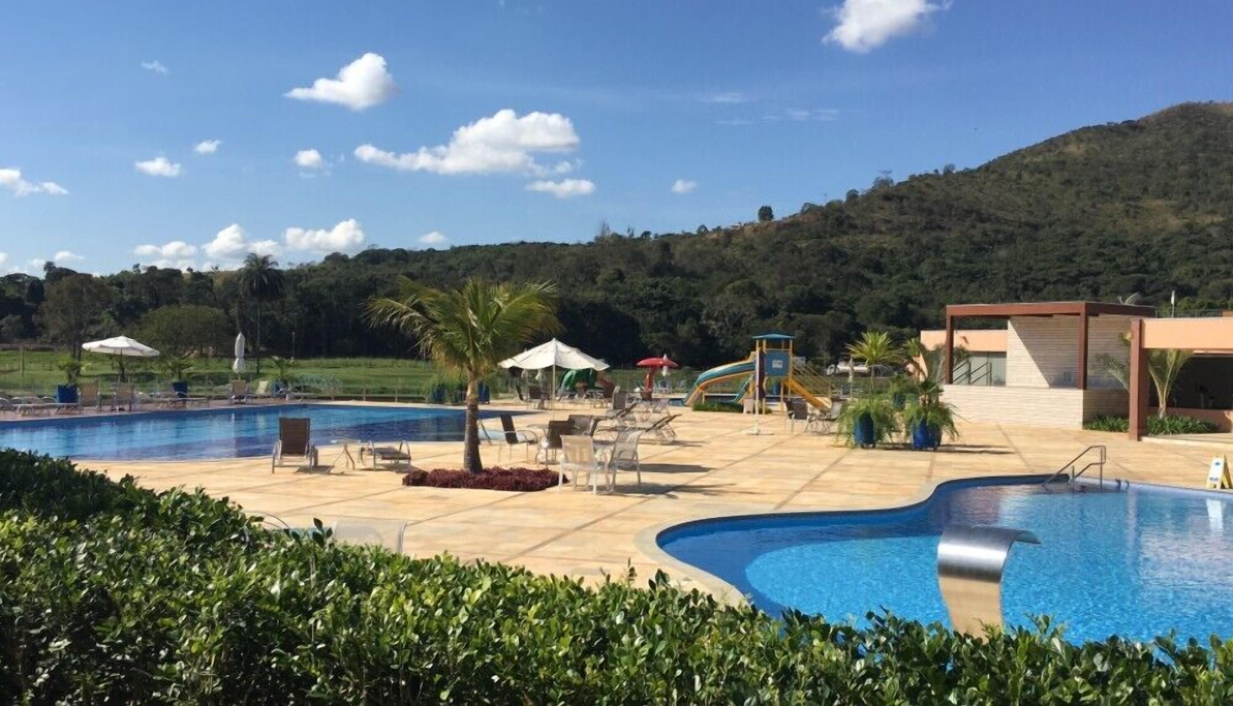 Uma área de piscina com espreguiçadeiras e guarda-sóis, cercada por vegetação e colinas.
