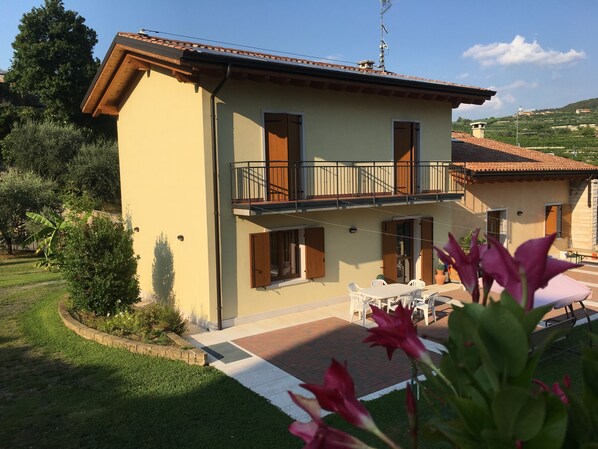 Uma casa de dois andares com varanda, um pátio com móveis de exterior e um espaço de jardim.