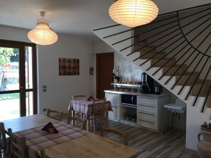 Uma área de refeições com uma mesa e cadeiras de madeira, uma cozinha com micro-ondas e uma escada com design exclusivo.