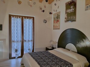 Um quarto com cama, janela com cortinas, parede com pôsteres e radiador.