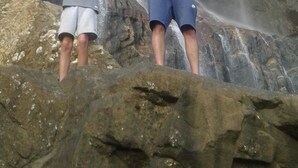 Two people standing on a rock with arms raised in front of a waterfall. - Nature's Rest (Ella)