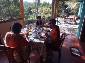 A dining area with a table set for four, surrounded by chairs, with a view of lush greenery and a building in the background.