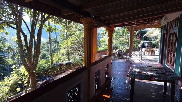 A covered outdoor area with a table and chairs, a view of trees and greenery, and a building with a tiled floor. - Nature's Rest (Ella)