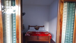 A narrow room with a wooden bed, a nightstand, and a wall-mounted lamp. - Nature's Rest (Ella)