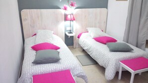 A twin room with two beds, each with a pink and grey pillow, a bedside table, and a nightstand. - Casa Grande (Constantina)