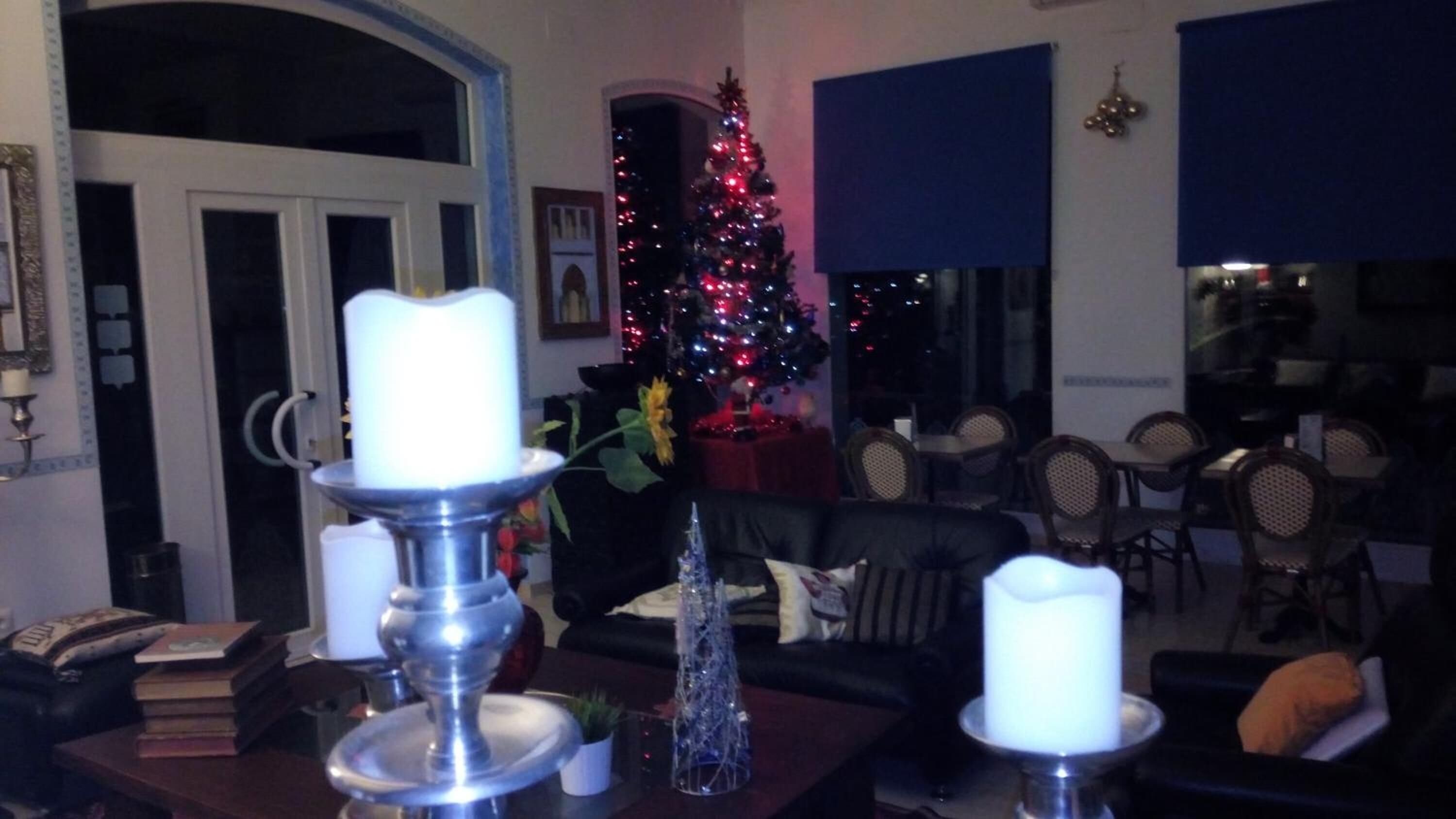 A living room with a Christmas tree, two lit candles, and a dining area with chairs and tables.