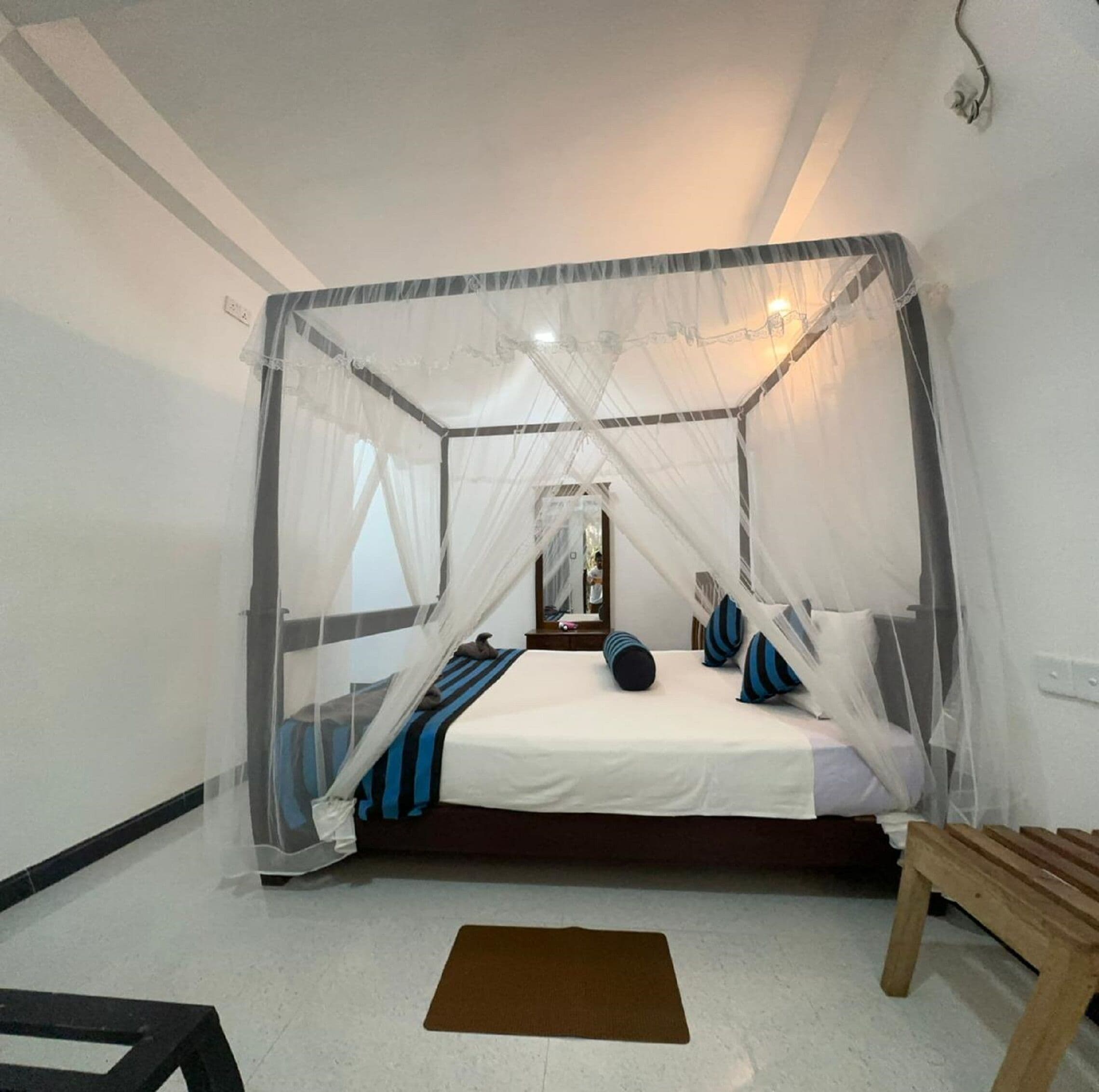 Un dormitorio con una cama con dosel, una mesita de noche, un espejo y un banco de madera.