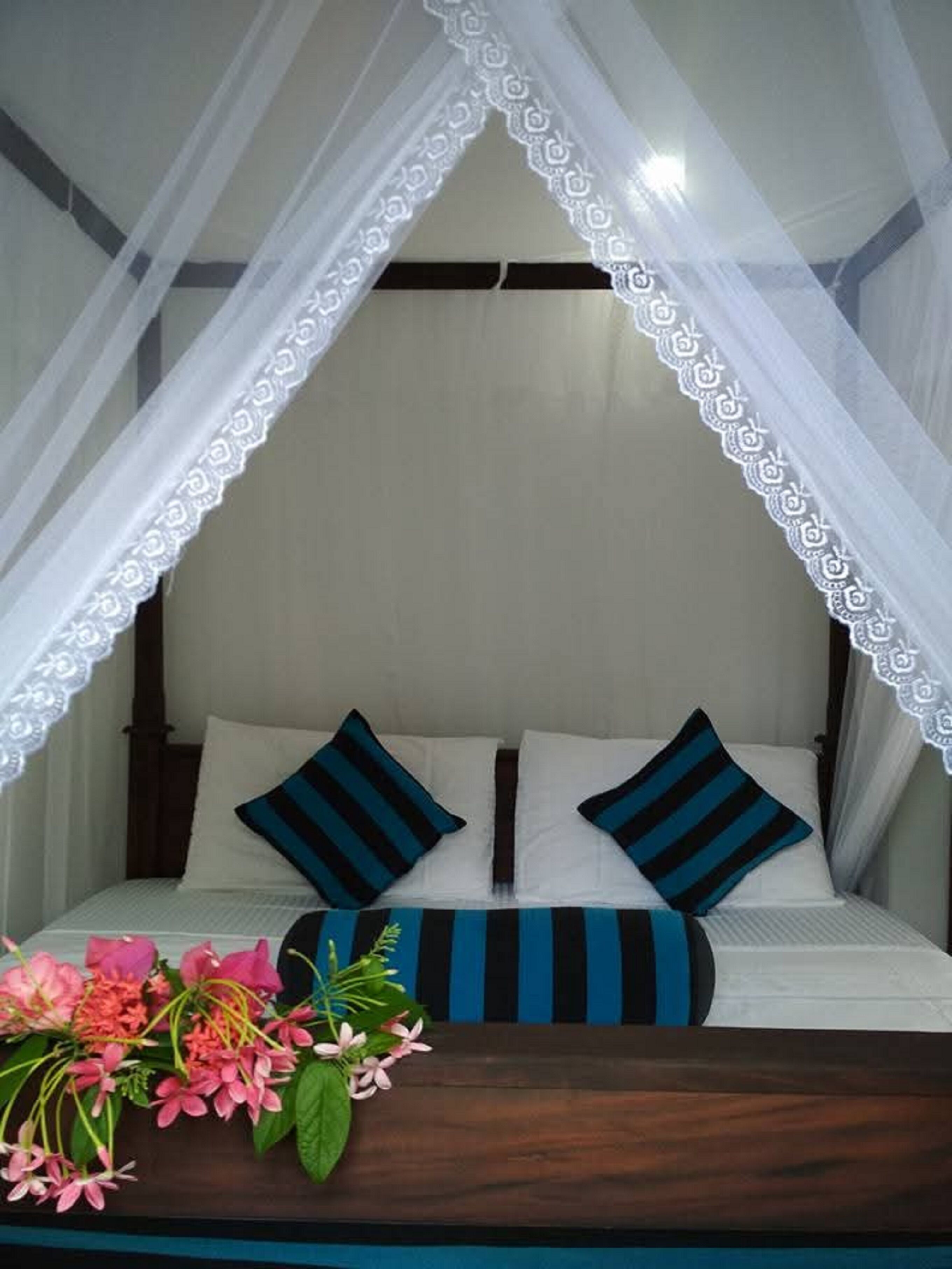 Een bed met hemelbed, kussens en een bloemstuk.