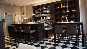Een moderne bar met een geruit vloertje, barstoelen en schappen met glazen.