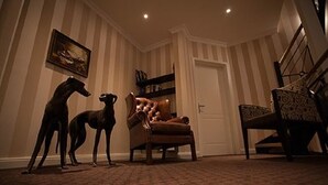 Een kamer met gestreept behang, een houten stoel, een bank en een schilderij aan de muur.