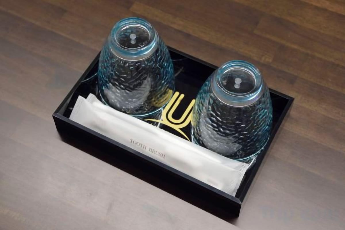 A black tray with two glass containers and a gold object on a wooden floor.