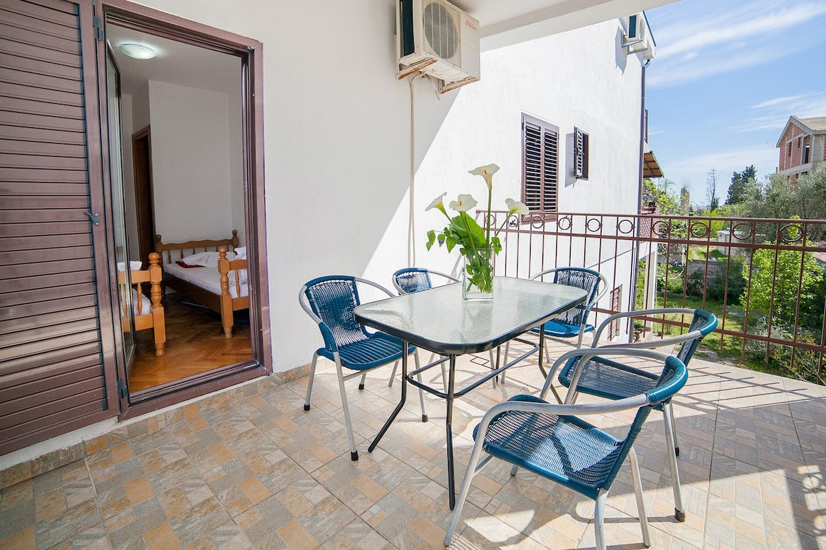 Un balcon avec une table et des chaises, un pot de fleurs et une vue sur les environs.