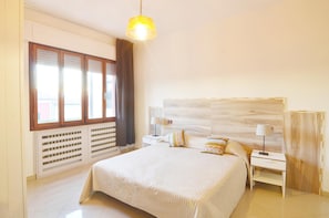 A bedroom with a large bed, a nightstand, a lamp, a window with curtains, and a radiator.